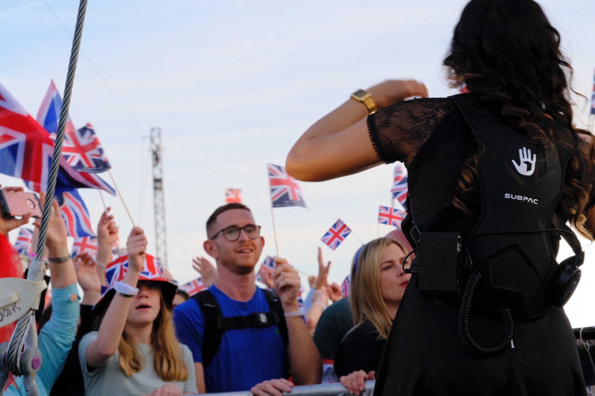 An individual enjoying the concert experience using a SUBPAC wearable technology, while a BSL interpreter communicates the musical performance in the background